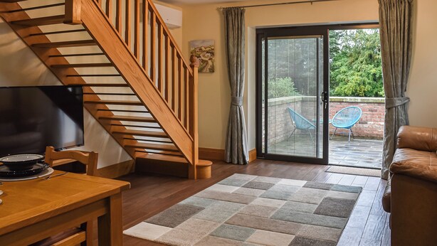 A modern living room with a wooden staircase, a dining area, and a sliding glass door leading to a patio with a blue chair. - Intimate and inviting, this couples retreat is a cosy haven for two. (South Kilvington, near Thirsk)