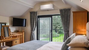 A bedroom with a bed, a desk, a television, and a view of a garden through a sliding door. - Intimate and inviting, this couples retreat is a cosy haven for two. (South Kilvington, near Thirsk)