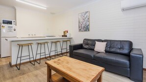 Una sala de estar moderna con un sofá de cuero negro, una mesa de centro de madera y una cocina con taburetes.
