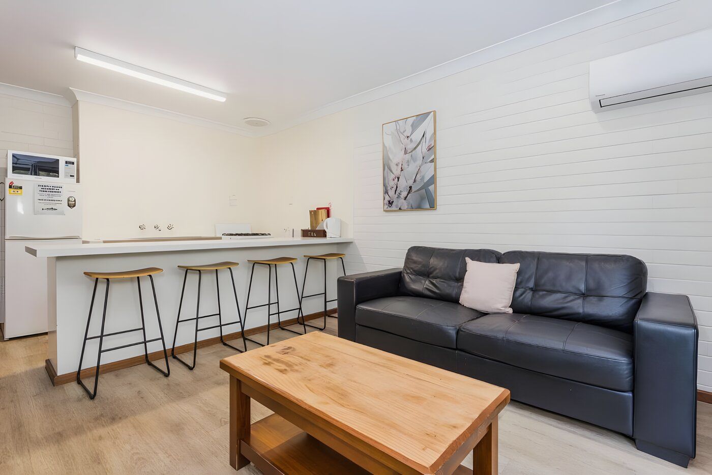 Un espace de vie moderne comprenant une cuisine, un canapé en cuir noir, des tabourets en bois et une table basse en bois.