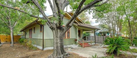 A single-story house with a large tree in front, a covered porch, and a small front yard with mulch and plants.