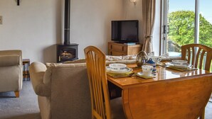 A cozy room with a wooden dining table set for two, a television, a fireplace, and a window with a view of greenery. - 1 bedroom accommodation in Tatham, near Lancaster (Tatham, near Lancaster)
