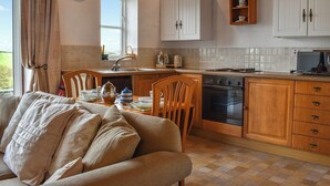 A cozy kitchen with wooden cabinets, a dining table set for two, and a clock on the wall. - 1 bedroom accommodation in Tatham, near Lancaster (Tatham, near Lancaster)