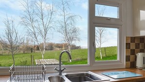Une cuisine avec une grande fenêtre, un évier et une bouilloire posée sur le plan de travail.