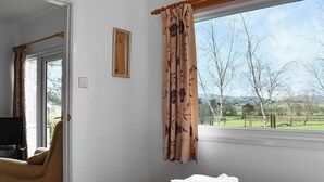 Une chambre à coucher avec un lit, une chaise, une fenêtre avec des rideaux et une vue sur l’extérieur.