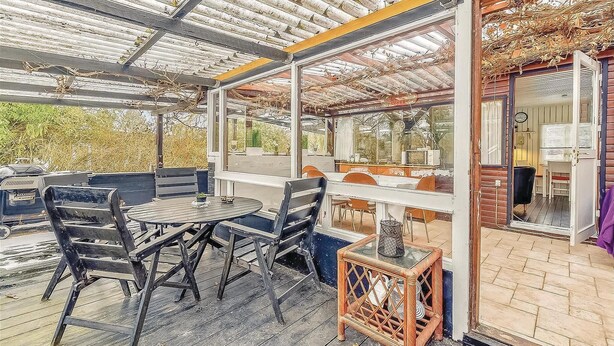 An outdoor patio with a table and chairs, a wicker stool, and a wooden deck. - Nice home in Sydals with WiFi (Sydals)