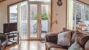 Ein Wohnzimmer mit einem braunen Ledersofa, einem Flachbildfernseher auf einem Schrank und einer Schiebetür zum Balkon.