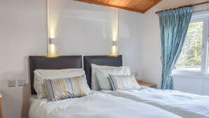 Ein Doppelbett mit weißer Bettwäsche und gestreiften Kissen, ein Holz-Kopfteil und ein Fenster mit blauen Vorhängen.