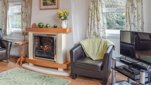 Ein gemütliches Wohnzimmer mit Kamin, Ledersessel, Fernseher und einem Kaminumbau mit Dekorationen.