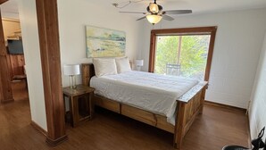 A bedroom with a wooden bed, a ceiling fan, a window, and a painting on the wall. - Stenson Hollow Lake Condo (Muscle Shoals)