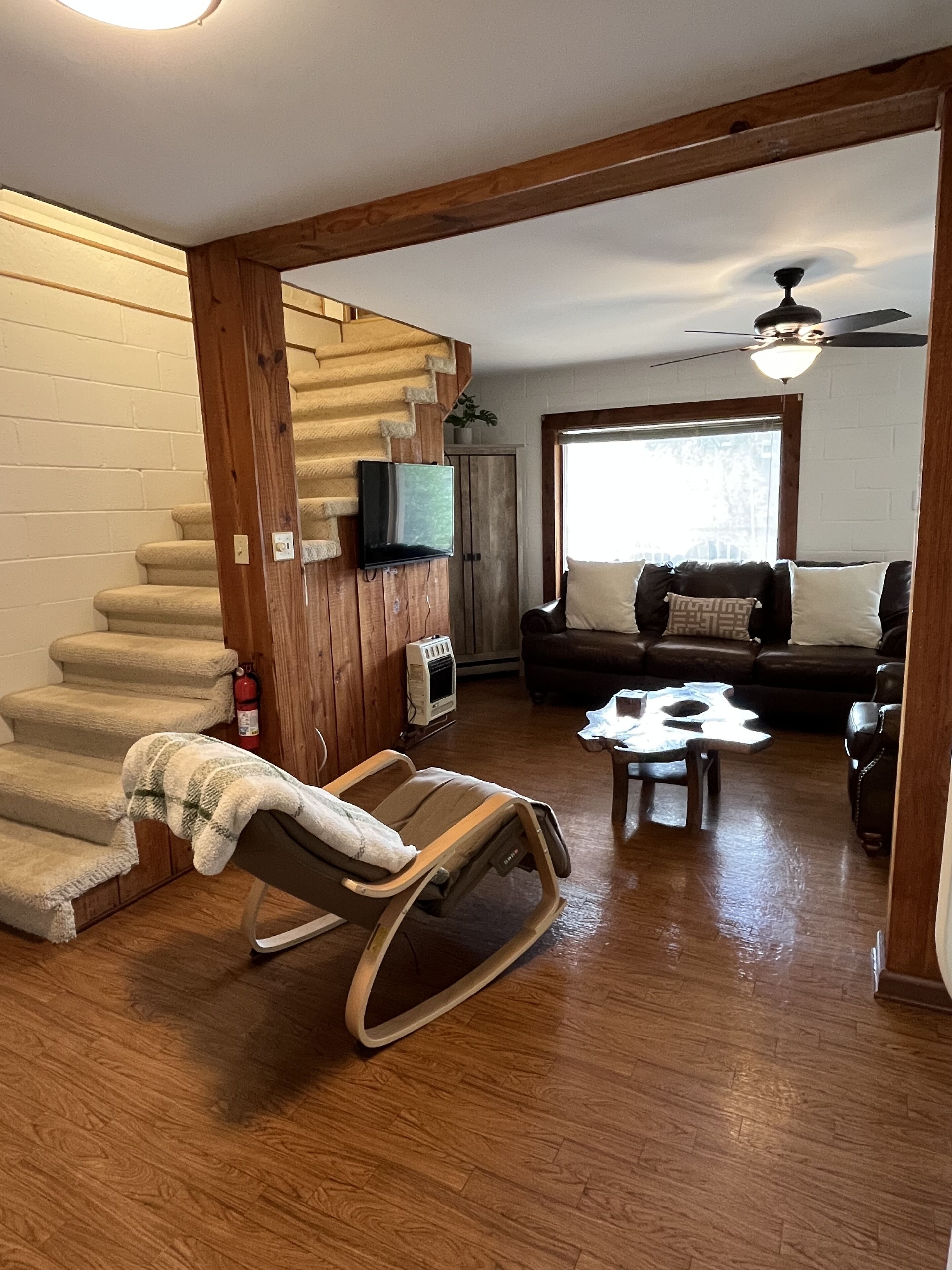 A living room with a wooden staircase, a rocking chair, a sofa, and a ceiling fan.