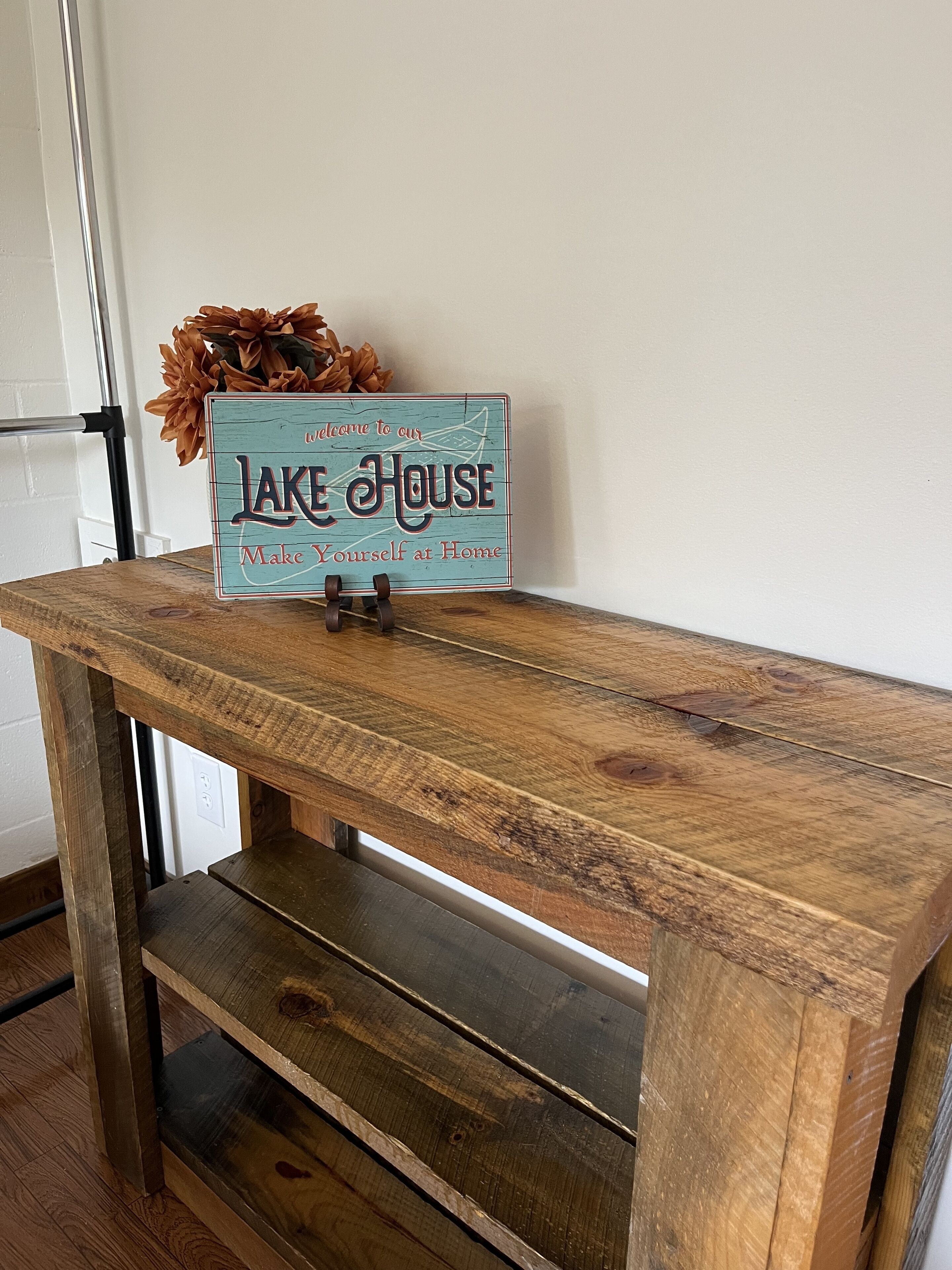 A rustic wooden table with a sign that reads "Welcome to our Lake House Make Yourself at Home."
