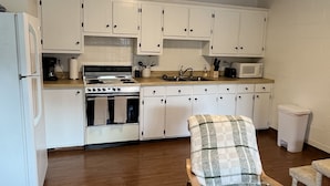A kitchen with white cabinets, a stove, and a microwave. There is a chair with a plaid cushion. - Stenson Hollow Lake Condo (Muscle Shoals)
