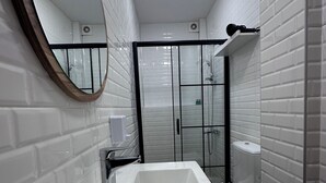 Une salle de bain moderne avec un grand lavabo rectangulaire, un miroir rond et une douche séparée par des parois en verre.