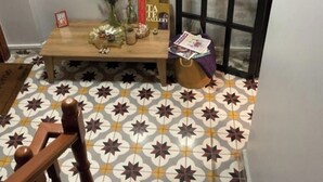 Une pièce avec un sol à motifs, une table en bois agrémentée d’objets décoratifs, un tableau encadré au mur et une porte avec un panneau de verre.