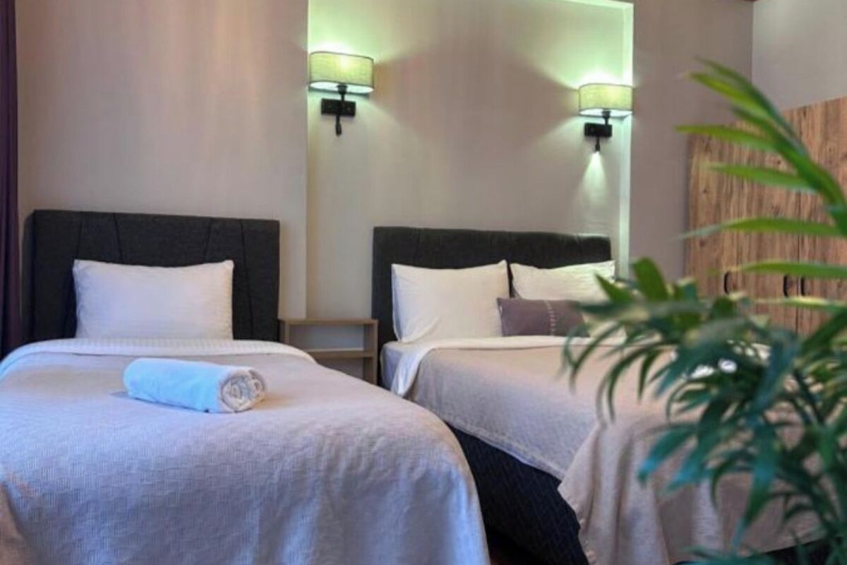 A hotel room with two beds, wooden ceiling, wall-mounted lamps, and a potted plant.