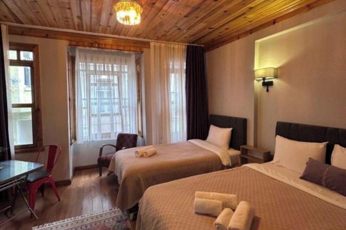 A hotel room with wooden ceiling, two beds, a desk, and a chair.