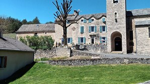A stone building with a bell tower, a grassy lawn, and a stone wall. - Gîte Philomène Dans Ancien Presbytère - 2 Pers - à St Georges de Lévéjac (Massegros Causses Gorges)