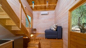 A compact wooden cabin with a sofa, a small table, and a staircase leading to a loft area.