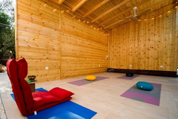 A wooden room with a ceiling fan, wooden walls, and exercise mats on the floor.