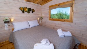 A wooden cabin bedroom with a bed, pillows, a window, and wall-mounted lights.