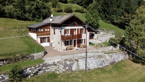 A two-story chalet with a balcony, stone retaining wall, and a stone staircase leading to the entrance.