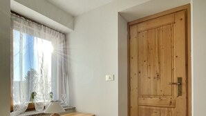 A room with a wooden dresser, a window with sheer curtains, a wooden door, and tiled flooring.