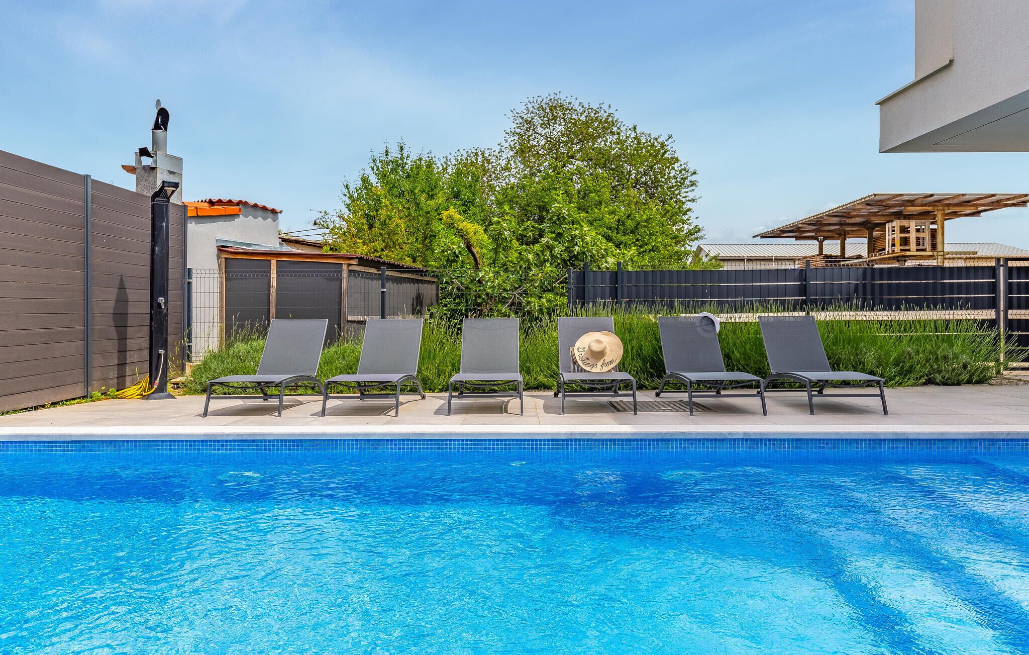Une piscine avec quatre chaises longues et un grand arbre en arrière-plan.