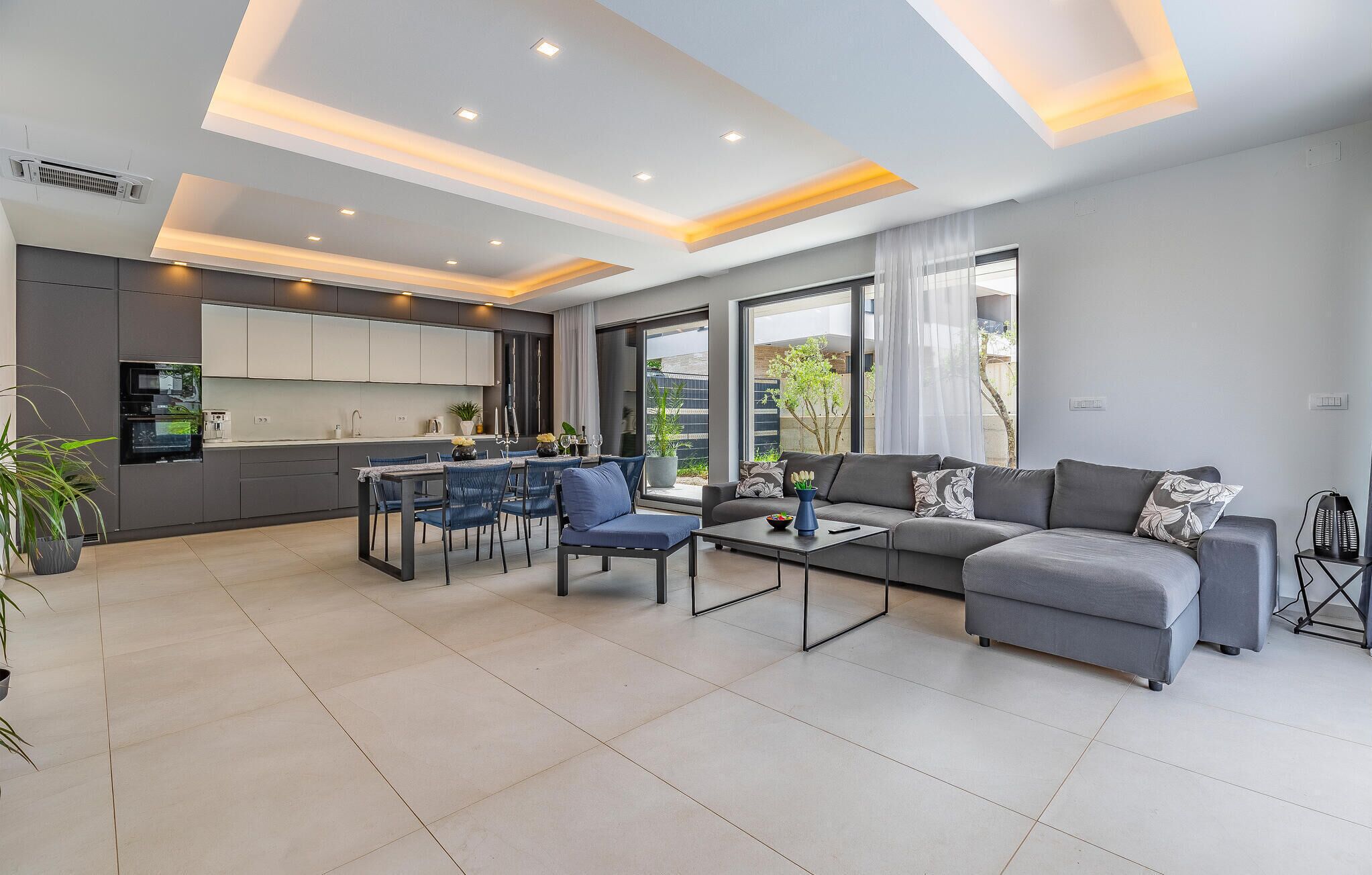Un salon moderne avec un canapé gris, une table basse et un coin repas avec des chaises bleues.
