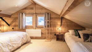 Un dormitorio ático acogedor con dos camas, paredes de madera y vistas a montañas nevadas a través de las ventanas.