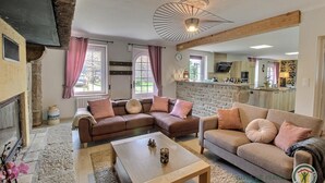 Een gezellige woonkamer met twee banken, een bijzettafeltje en een open haard. In de achtergrond is een stenen muur en een keuken te zien.
