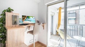 A modern apartment with a wooden desk, a laptop, a large beach-themed TV, and a view of a balcony with yellow curtains. - Stunning apartment in El Campello with WiFi (El Campello)