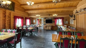 A wooden interior with multiple tables and chairs, a television mounted on the wall, and a stone-tiled floor. - 1 bedroom cozy home in Grue Finnskog (Grue Finnskog)