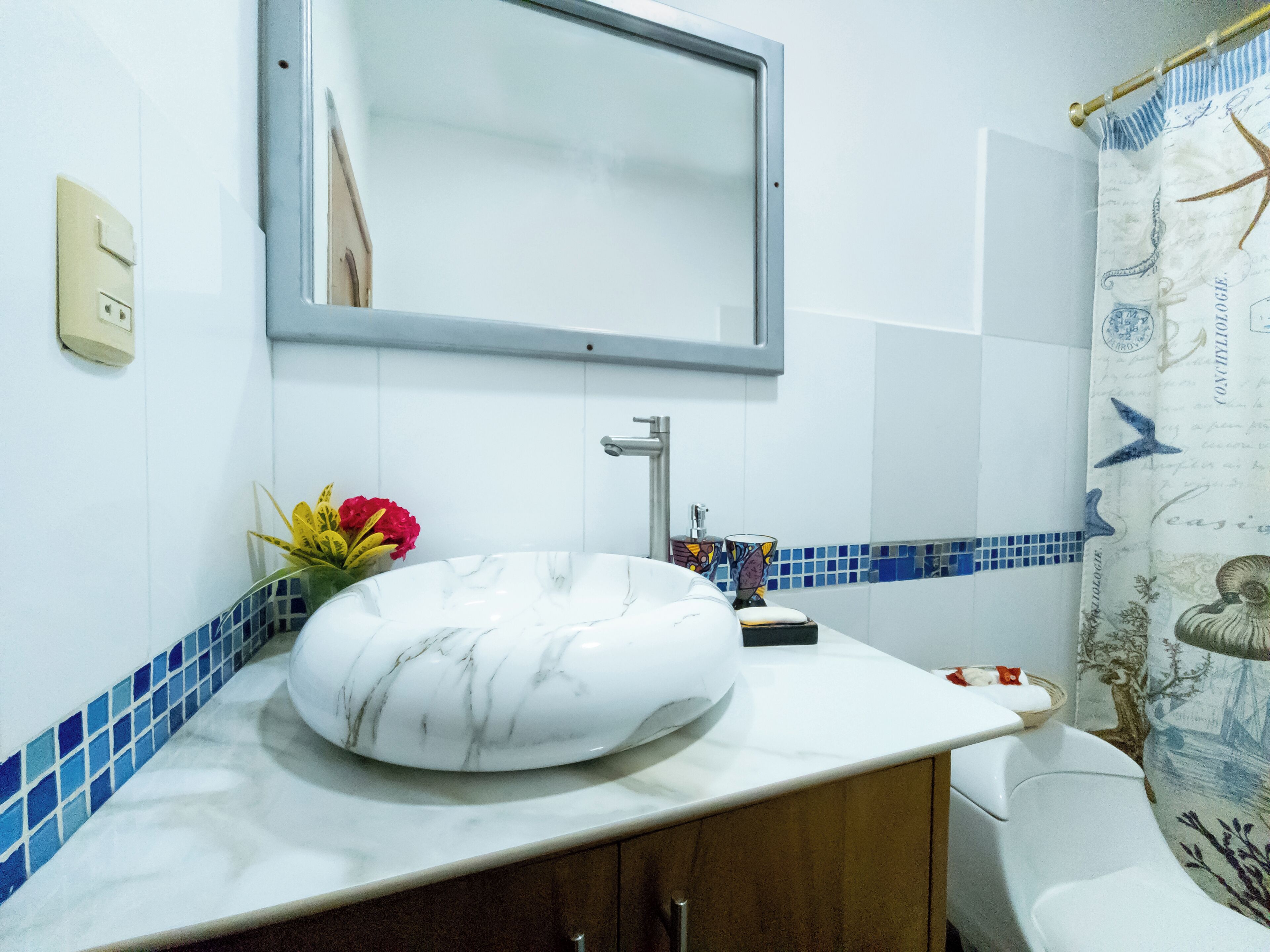 A bathroom with a white marble sink, a mirror above it, and a blue-tiled shower area.