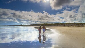 Une plage avec un ciel dégagé et un couple se promenant sur le sable mouillé.