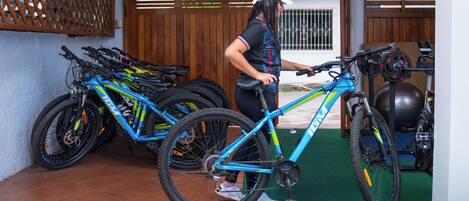 Una mujer ajustando una bicicleta azul en un espacio exterior techado con varias bicicletas y una bicicleta estática.