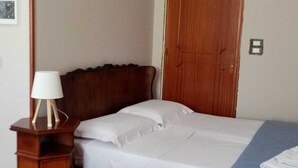 Een slaapkamer met een houten hoofdbord, een nachtkastje met een lamp, een bed met wit beddengoed en een blauwe deken op de vloer.