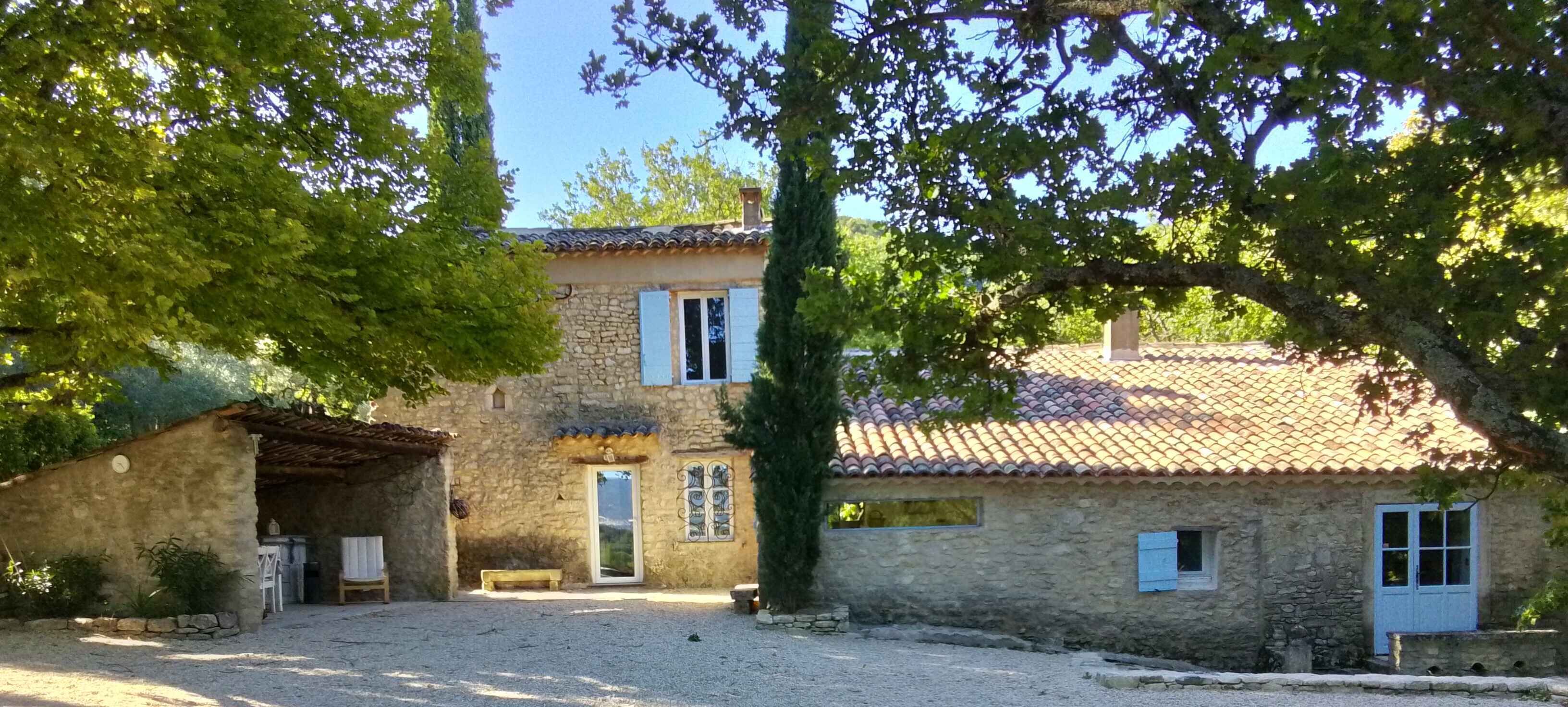 A stone house with a tiled roof, a small porch, and a gravel driveway.