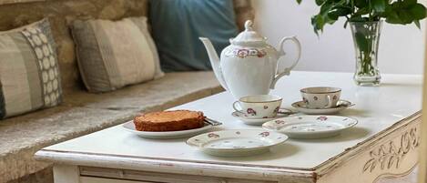 A table set with a teapot, cups, saucers, and a plate with toast, placed on a window seat with a view of greenery.