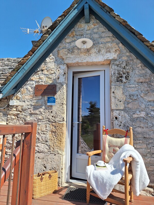 Un edificio de piedra con techo de tejas, una silla de madera con una toalla y una puerta con un letrero.