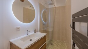 A modern bathroom with a white sink, wooden vanity, a round mirror, and a glass-enclosed shower. - Appartement de Charme Aix en Provence (Aix-en-Provence)