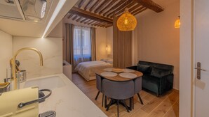 A compact hotel room with a kitchenette, a bed, a dining area, and a dark-colored sofa. - Appartement de Charme Aix en Provence (Aix-en-Provence)