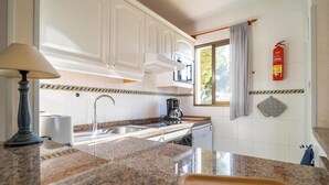 Una cocina con gabinetes blancos, encimera de granito, cafetera, lavamanos y extintor.