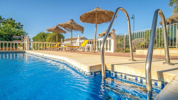 Una piscina con agua azul cristalina, rodeada de sillas de descanso y sombrillas de paja.