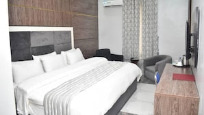 A modern hotel room with a large bed, a desk, a chair, and a TV. - Esporta Suites Hotel GRA (Lagos)