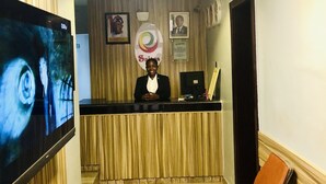 A reception desk with a television, a framed logo, and a framed portrait on the wall. - Esporta Suites Hotel GRA (Lagos)