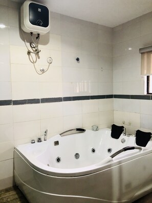 A bathroom with a large bathtub, a wall-mounted heater, and a window with blinds. - Esporta Suites Hotel GRA (Lagos)