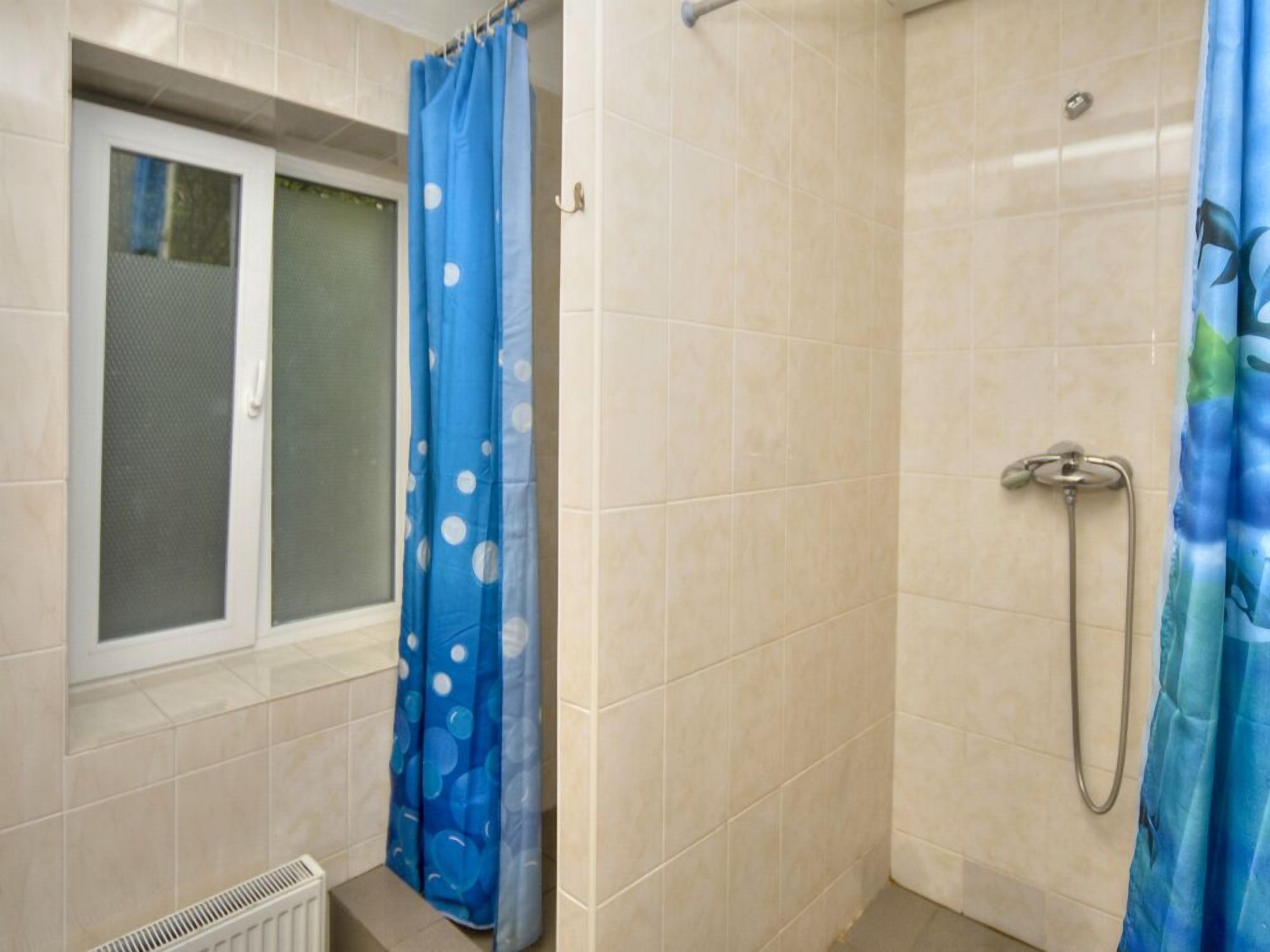 A bathroom with a shower, a window with a frosted glass door, and a vent.