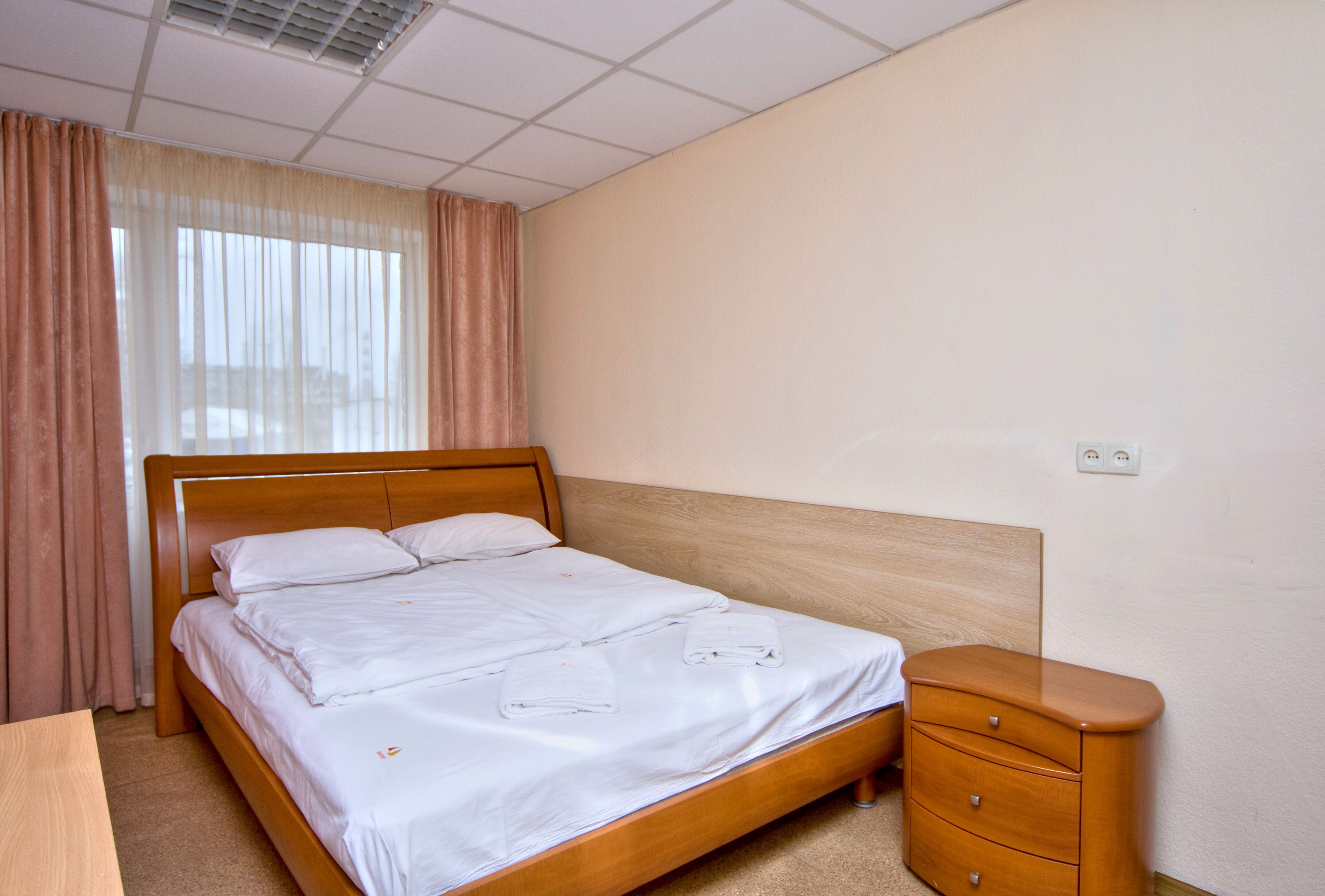 Una cama bien hecha con sábanas blancas, un cabecero de madera y una mesita de noche de madera con cajones.