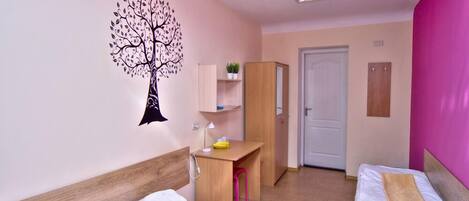 A hotel room with two beds, a desk, a chair, a wardrobe, a door, and a wall decoration of a tree.